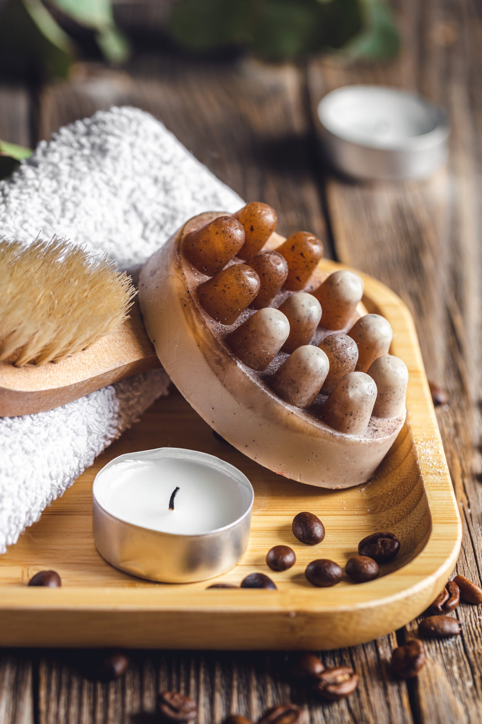 Spa composition with coffee massage scrub soap, coffee beans, brush and candle on a wooden surface.